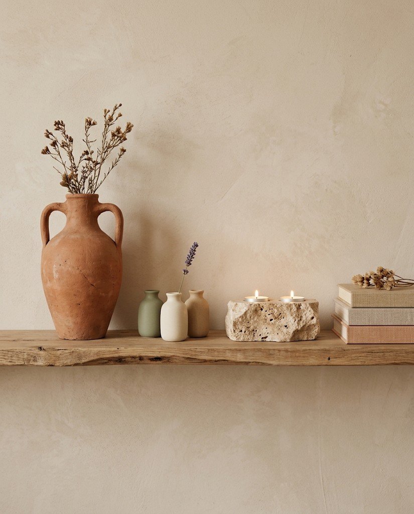 A wooden shelf styled with a terracotta vase, ceramic bud vases, a travertine tea light holder and linen books